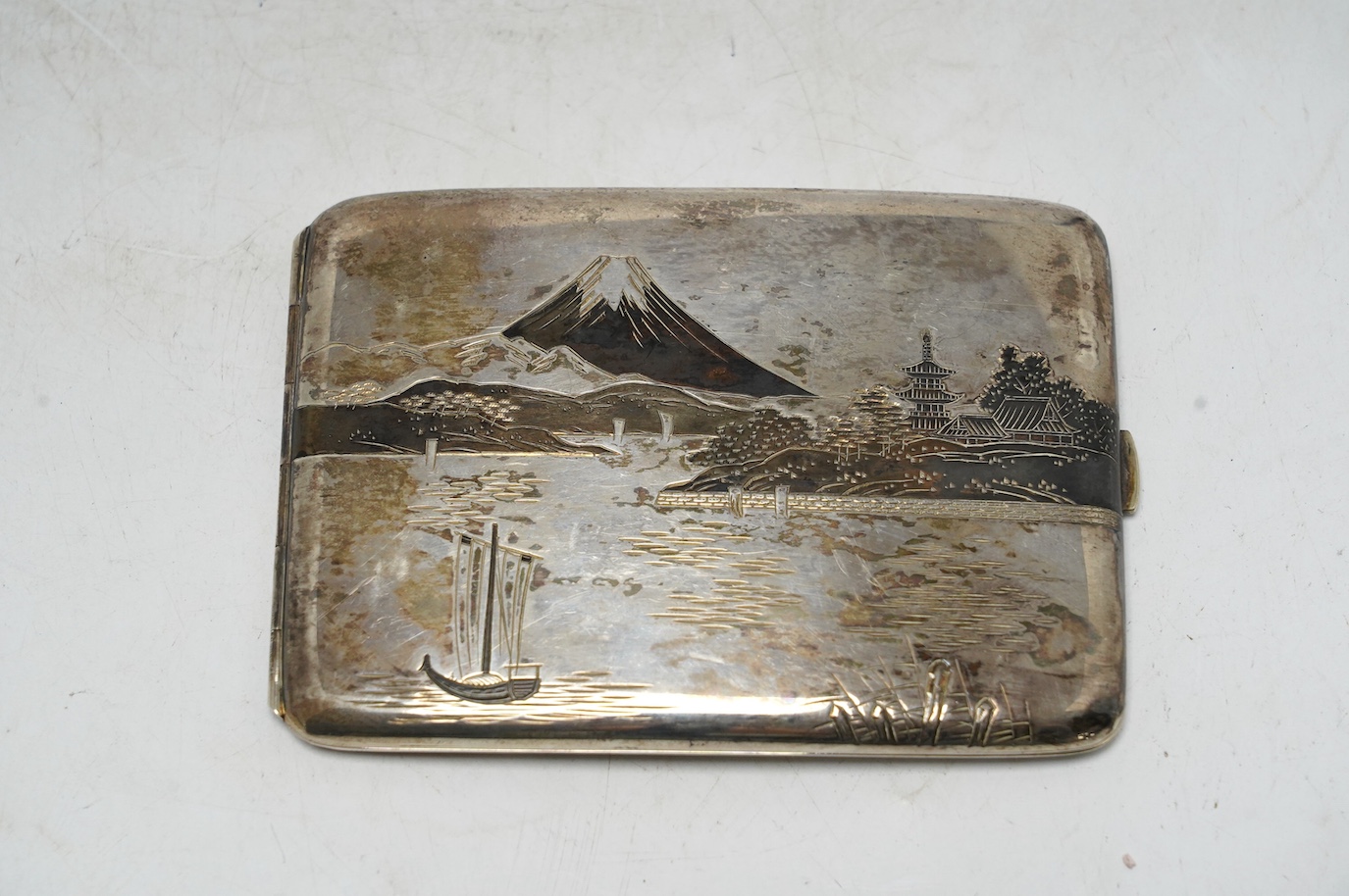 A white metal (stamped) and dark patinated Japanese silver cigarette case, decorated with a view of Mount Fuji, signed, 11cm, gross weight 113 grams. Condition - fair